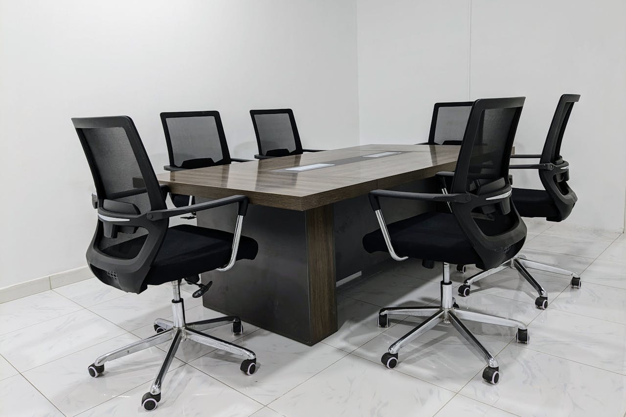 A neat and minimalistic conference room setup with black mesh chairs around a dark wooden table.